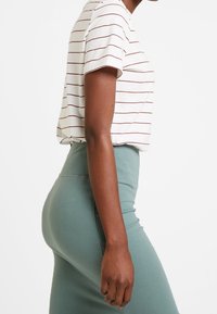 Chemise à manches courtes rayée couleur crème avec des lignes bordeaux, associée à une jupe crayon verte. Présente une coupe décontractée et une texture de tissu lisse.