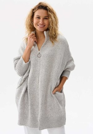 Jasnoszary, oversize sweter dzianinowy z kołnierzem na suwak, długimi rękawami, ściągaczami przy mankietach i kieszeniami z przodu. Teksturowany materiał o przytulnym wyglądzie.