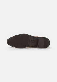 Brown leather shoe sole with textured black rubber, featuring a geometric tread pattern and branding details. Flat design with rounded edges.