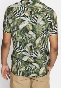 Kortærmet skjorte med sort baggrund, store grønne og lyseblå palmebladsmønstre samt hvide striber; letvægtsstof.