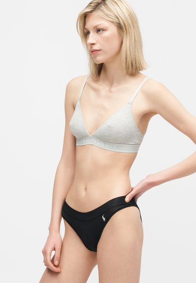 Ξανθιά γυναίκα που φοράει γκρι bralette Ralph Lauren και μαύρο εσώρουχο με λογότυπο Polo, στέκεται με το χέρι στη μέση μπροστά σε λευκό φόντο.