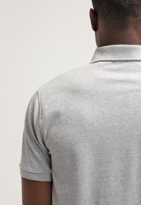 Grå polo skjorta i texturerad tyg, med klassisk krage och korta ärmar, sedd bakifrån. Minimal detaljering.