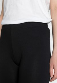 Leggings noirs en tissu extensible avec une texture lisse, présentant une taille haute et une silhouette ajustée.