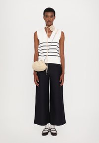 Pull sans manches blanc à rayures marines, pantalon large marine, sac à épaule beige texturé, et chaussures à brides marron sur des chaussettes blanches.