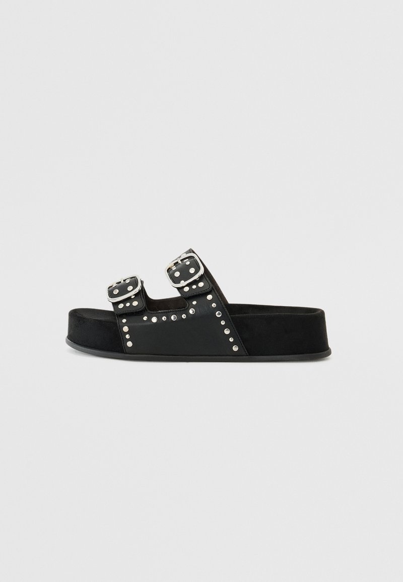 Black slide sandal with dual buckles, studded accents, and a textured material. Features a flat sole and sturdy construction.