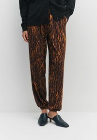 Hnedo-oranžové nohavice so zvieracím vzorom, voľným strihom a zúženými manžetami, čierne šľapky s hrubým podpätkom. Kombinované s čiernym kardigánom.