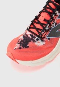 Helle korallenfarbene Laufschuhe mit einem strukturierten Obermaterial, das schwarz-weiße Muster aufweist, flachen Schnürsenkeln und einer massiven weißen Zwischensohle.