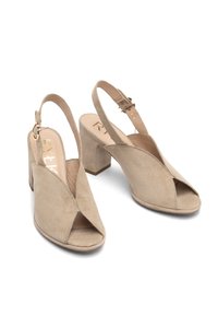 Sandale bej din suede cu vârful deschis, cu toc gros, având un design cu decupaj și curea ajustabilă pentru gleznă. Textură netedă, accente minime.