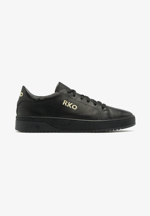 Baskets basses en cuir noir avec des lacets noirs et un logo "RKO" doré sur le côté et le talon, semelle plate, vue latérale sur fond blanc.