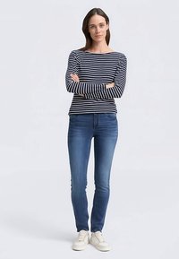 Tengerészkék és fehér csíkos hosszú ujjú póló, kék szűk farmerrel és fehér sportcipővel viselve. Az öltözék laza szabású és egyszerű kialakítású.