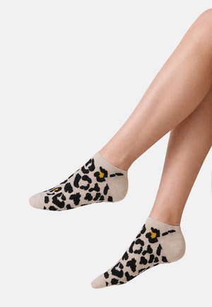 Legs wearing beige ankle socks with black and yellow leopard print pattern against a plain background.