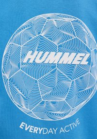 Blaues Baumwoll-T-Shirt mit weißem Grafikdesign eines Fußballes und wellenförmigen Linienmustern. Unten steht der Text "HUMMEL" und "EVERYDAY ACTIVE".