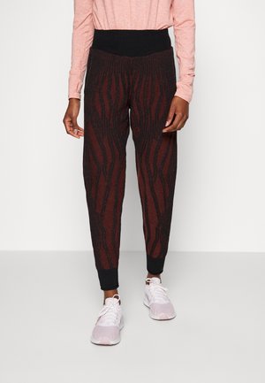 Person wearing high-waisted black and dark red patterned jogger pants with black cuffs and light pink sneakers.