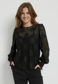 Černá krajková blůza s květinovými vzory, dlouhými nabíranými rukávy a kulatým výstřihem. Textil má textura a jemný lesk.