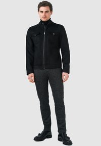 Svart mockajacka med ståkrage, dragkedja och två bröstfickor. Matchat med strukturerade mörkgrå byxor och svarta skor.