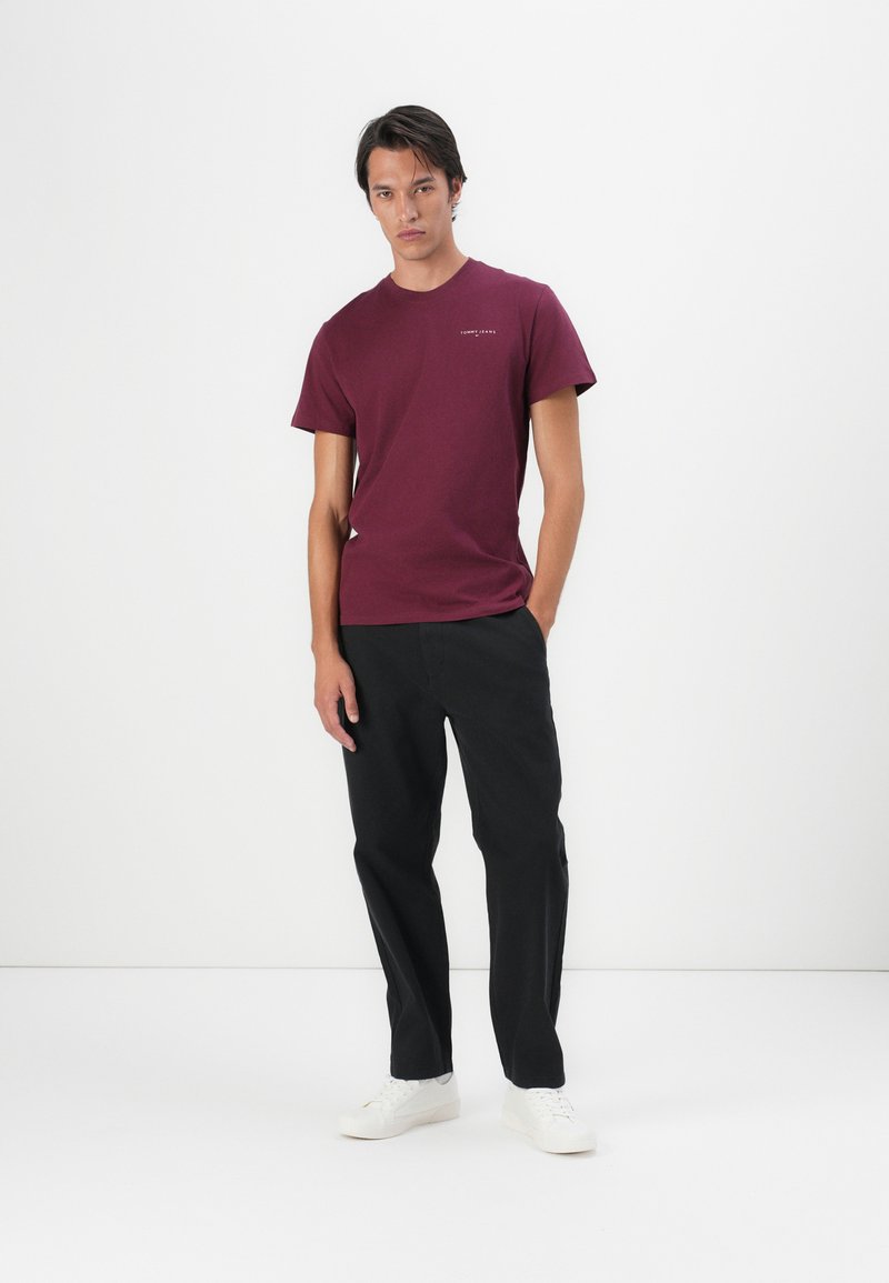 Burgunderfarbendes Baumwoll-T-Shirt mit kurzen Ärmeln und Rundhalsausschnitt, kombiniert mit schwarzen Hosen und weißen Sneakers. Einfaches Design, ohne Muster.