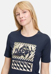 Granatowa bawełniana koszulka z krótkim rękawem z grafiką, która zawiera napis "HAPPY" oraz faliste akcenty w kolorze kremowym i złotym.