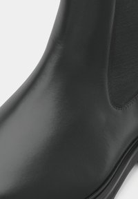 Melni ādas potītes zābaki ar gludu apdari, elastīgu sānu paneli, apaļu purngalu un teksturētu auduma akcentu. Zemi gumijas zābaki.