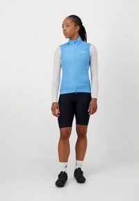 Vestă de ciclism albastru deschis cu fermoar integral, combinată cu pantaloni scur�ți de ciclism negri. Vesta are mâneci lungi albe și un design slim fit.