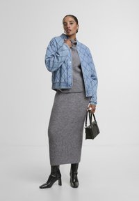 Kviltota gaiši zila bumbieru jaka, pelēcīgs ribots krekls, pelēcīgs adīts svārks, melni zābaki līdz potītei, tur mazu melnu rokassomu.