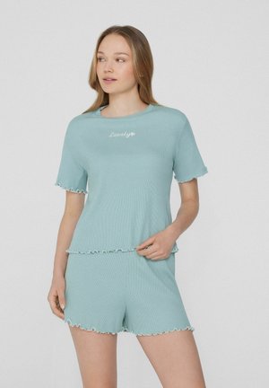 Ensemble de détente turquoise à côtes avec un ourlet volant sur le haut et le short, portant "Lovely" brodé en blanc sur la poitrine.