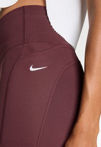 Maroon high-waisted leggings with textured fabric, featuring flat seams and a small white Nike logo on the side.
