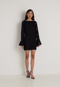 Melna mežģīņu kleita ar garām zvanu piedurknēm, pieguļošu siluetu un ziedu rakstiem. Pārī ar siksnām augstpapēžu kurpēm un somiņu.