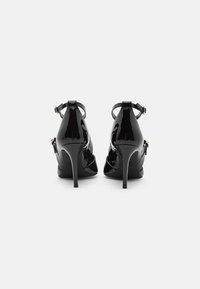 Escarpins en cuir verni noir avec des brides de cheville et des accessoires en or. Présentent une toe pointue et un talon aiguille élancé.