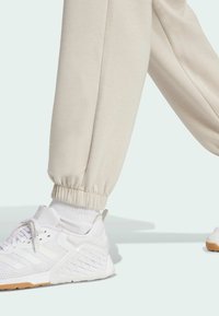Pantalones de chándal beige con puños acanalados, combinados con zapatillas deportivas blancas que presentan un diseño texturizado y suela de goma, con calcetines blancos visibles.