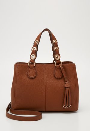 Sac à main en cuir marron texturé avec doubles poignées arrondies, œillets dorés, bandoulière longue détachable et détail à pompon sur fond blanc.