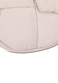 Borsa imbottita in tessuto beige chiaro con bordi cuciti. Presenta un logo "EXPATRIE" in rilievo, forma arrotondata e texture morbida.