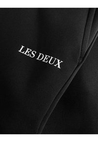 Tissu noir à la texture lisse avec le logo "LES DEUX" en impression blanche. Le design est minimaliste et contemporain, mettant l'accent sur la simplicité.