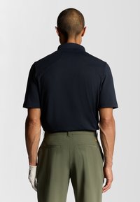 Marinblå kortärmad polo med krage, kombinerad med olivgröna byxor. Skjortan har ett slätt, strukturerat tyg och en avslappnad passform.