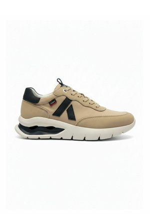 Beige sneaker met zwarte accenten, gewatteerde hiel, witte dikke zool met luchtkussen, veters aan de voorkant en een merklabel op het zijpaneel.