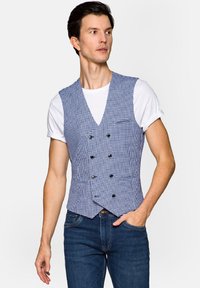 Niebieska i biała kamizelka w kratkę o strukturalnym kroju, z dekoltem w serek, podwójnym zapięciem z przodu i dwiema przednimi kieszeniami. Noszona na białej koszulce.