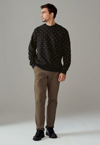 Felpa nera con motivo a V arancione, scollo tondo; abbinata a pantaloni beige chiaro e scarpe nere. Design semplice, vestibilità casual.