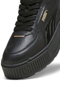 Baskets Puma noires avec semelle épaisse texturée, bout perforé, lacets noirs, et logo Puma doré sur le côté.