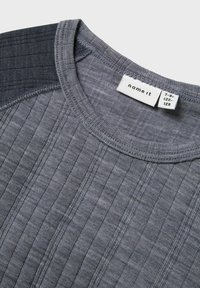 Grijze geribbelde T-shirt met een ronde halslijn, voorzien van een donkergrijs paneel op één schouder. Het label geeft aan merk "name it", maat 7-8 jaar.