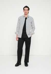 Čiernobiela vzorovaná košeľa s gombíkmi, dlhé rukávy, nosená cez čierne tričko s čiernymi nohavicami a čiernymi topánkami. Jednoduchý a moderný dizajn.