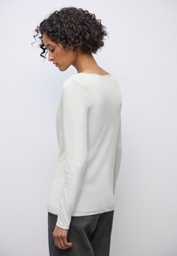 Haut gris clair à manches longues avec un col rond et une texture lisse, associé à un pantalon à carreaux sombres et texturé.