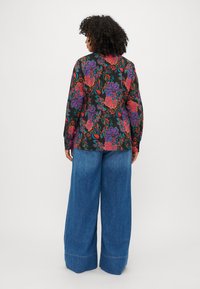 Blusa nera a maniche lunghe con un vivace motivo floreale multicolore, abbinata a pantaloni in denim blu a gamba larga con orlo ripiegato.
