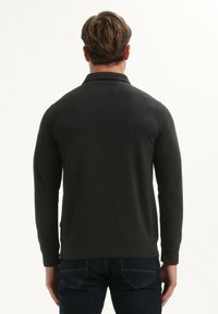 Donkergroen sweatshirt met lange mouwen, geribde manchetten en zoom, en een platte kraag. Gladde stof; minimale zichtbare branding aan de zijkant.