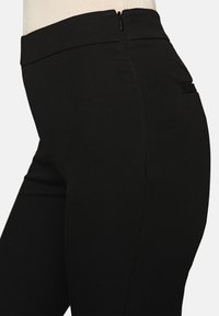 Svarta skräddarsydda byxor med ett mjukt tyg, hög midja, dragkedjeöppning på sidan och en diskret ficka på baksidan.