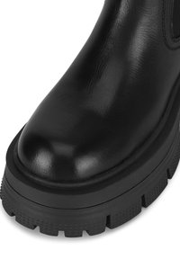 Czarny skórzany botek za kostkę o wysokim połysku, z masywną gumową podeszwą, zaokrąglonym noskiem oraz teksturowanym wzorem bieżnika na spodzie.