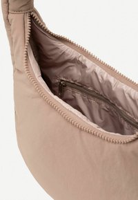 Mīksta, pasteļa rozā soma ar noapaļotu formu, strukturētu audumu un ar rāvējslēdzēju slēgtu iekšējo kabatu. Iekļautas dekoratīvās dūriena maliņās.