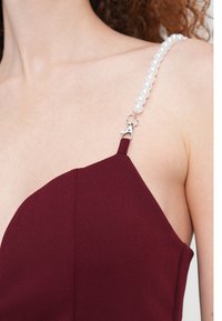 Μπορντό φόρεμα με εφαρμοστή σχεδίαση, υφασμάτινη υφή και λουράκι με πέρλα και ασημένια λεπτομέρεια κλίπς.