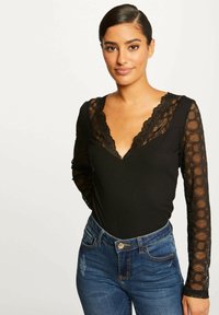 Body nero a maniche lunghe con dettagli in pizzo attorno al collo e alle maniche, abbinato a jeans in denim blu a vita alta.
