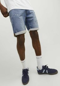 Shorts de mezclilla con un lavado azul claro, que presentan parches desgastados y dobladillos enrollados. Combinados con zapatillas navy y calcetines blancos de caña corta.