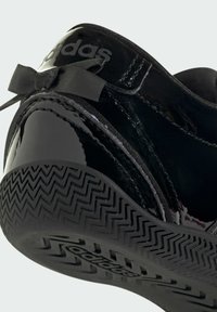 Baskets Adidas noires brillantes avec une semelle texturée, un ruban noir noué au talon et le logo Adidas sur l'onglet arrière du talon.