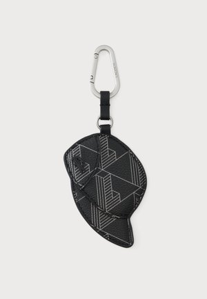 Porte-clés en cuir noir en forme de casquette avec des motifs géométriques, attaché à un mousqueton argenté étiqueté Lacoste.